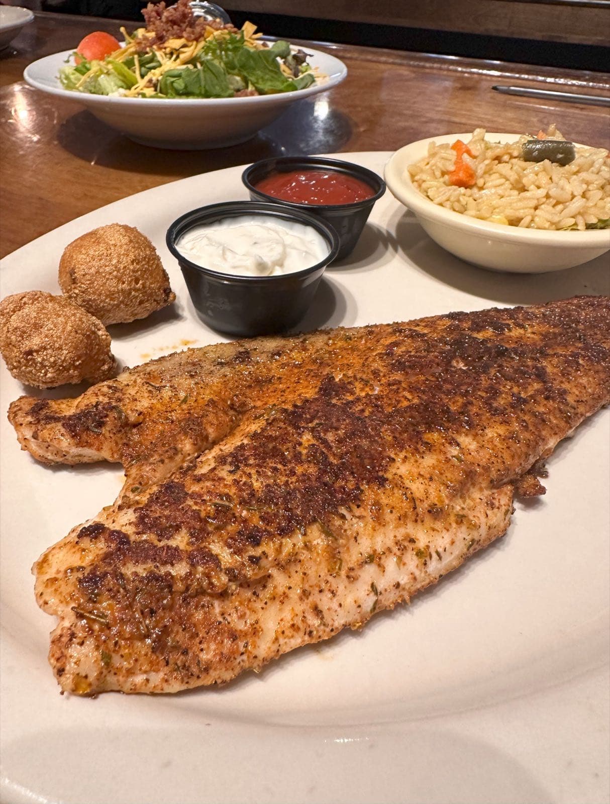 Blackened fish fillet with hushpuppies, rice pilaf, and dipping sauces