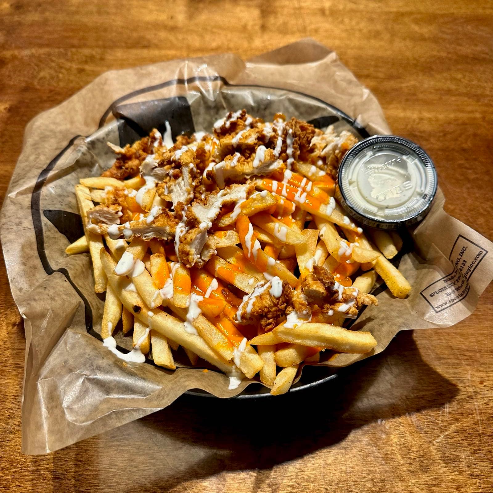Basket of crispy fries topped with fried chicken bites, buffalo sauce, and ranch drizzle.