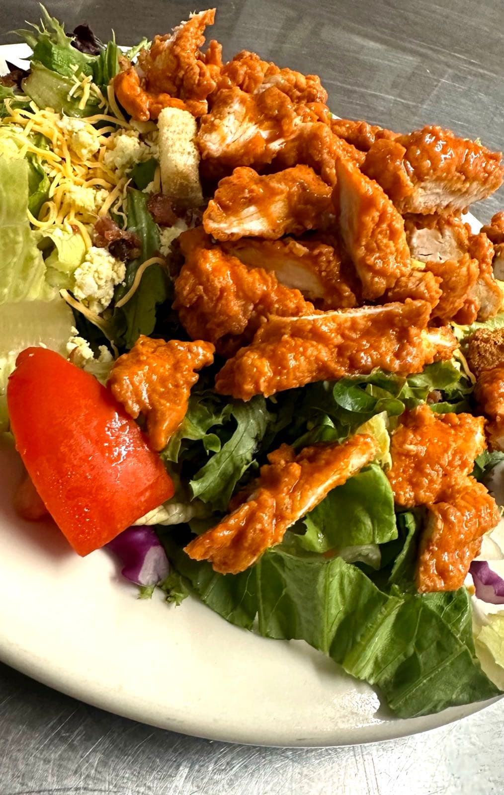 Sliced buffalo chicken tenders over a mixed greens salad with shredded cheese, blue cheese crumbles, tomato wedge, and red onion.