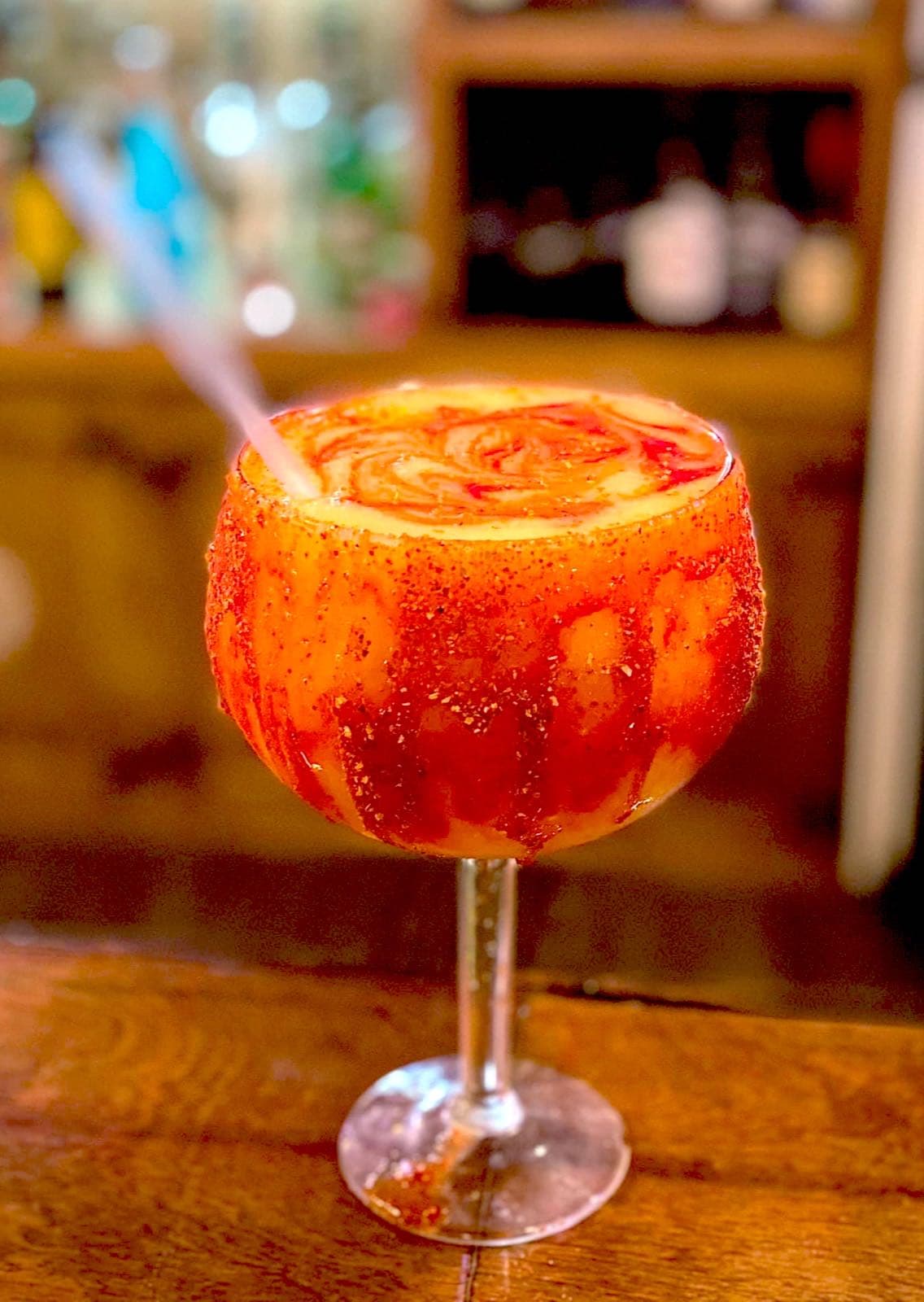 A chili-tajín-rimmed cocktail with a swirled orange and cream finish, served in a stemmed goblet at the bar.