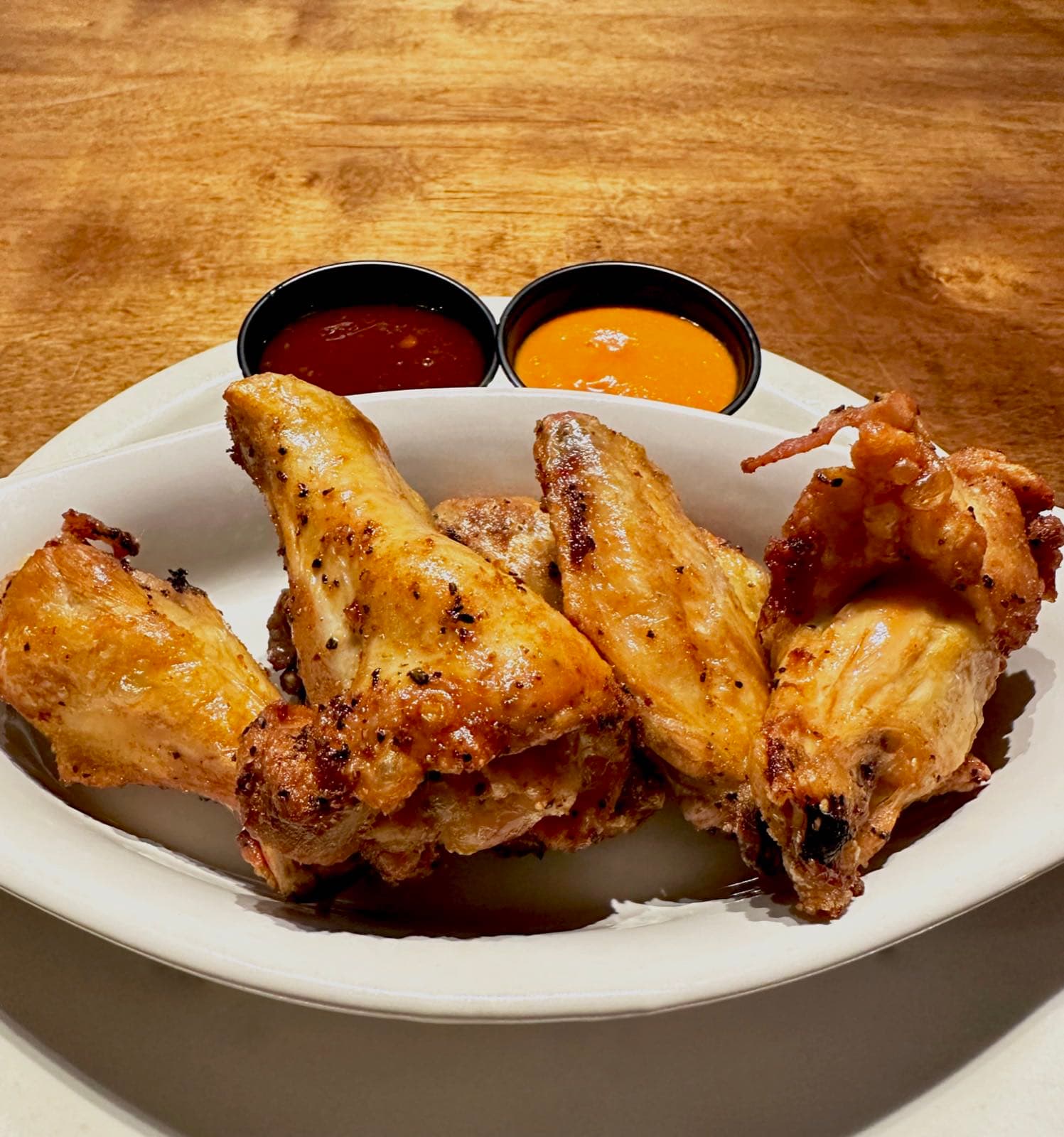 Golden, crispy jumbo chicken wings served with red and orange dipping sauces.